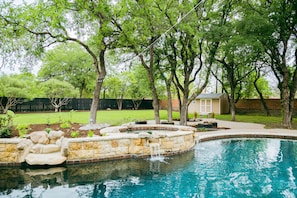 A backyard with a swimming pool, stone steps, and a small waterfall.