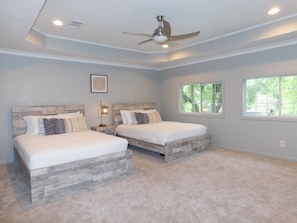 A bedroom with two beds, a ceiling fan, a window, and a nightstand with a lamp.