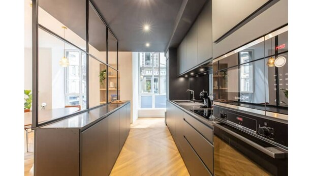 Une cuisine moderne dotée d’un îlot central, d’appareils électroménagers intégrés et offrant une vue sur l’extérieur.