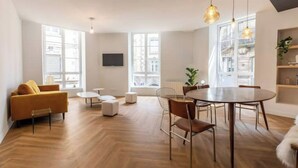 Un salon moderne avec un canapé, une table à manger et des chaises, ainsi que de grandes fenêtres.