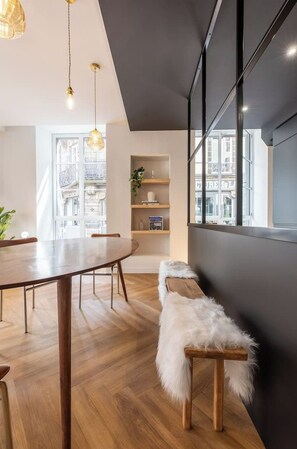 A modern dining area with a wooden table and chairs, a fur-covered bench, and pendant lighting.