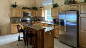 A kitchen with wooden cabinets, a stainless steel refrigerator, a microwave, and a ceiling fan. - Luxury Living with beautiful ocean and sunset views (Frederiksted)