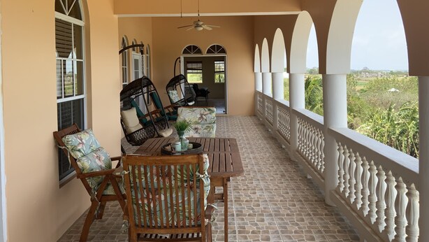 A covered patio with a table and chairs, a ceiling fan, and a view of greenery. - Luxury Living with beautiful ocean and sunset views (Frederiksted)