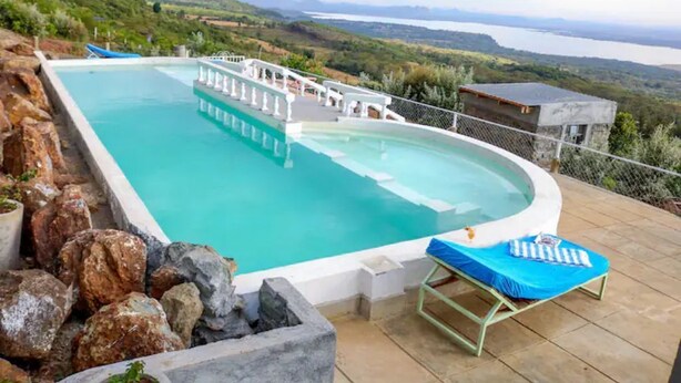 A rectangular pool with a hot tub, surrounded by rocks and a lounge chair. - Cabin in the Farm - Peach (Nakuru)