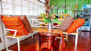 A room with a red floor, white furniture, and a green wall. There is a table with a vase of flowers and striped cushions. - Cabin in the Farm - Peach (Nakuru)