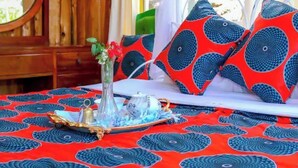 A bed with red and blue patterned bedding, a vase with flowers, and a tray with a teapot and cups. - Cabin in the Farm - Peach (Nakuru)