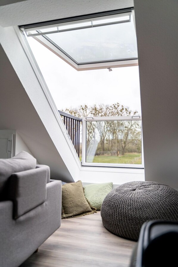A modern loft bedroom with a skylight, a gray sofa, and a knitted pouf.
