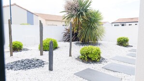 A courtyard with white gravel, small bushes, and a palm tree. - Beautiful holiday home 7 minutes from the beach in Brem sur Mer (Brem-sur-Mer)