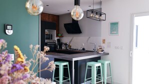 A modern kitchen with a central island, green bar stools, pendant lighting, and a visible smoke hood. - Beautiful holiday home 7 minutes from the beach in Brem sur Mer (Brem-sur-Mer)