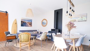 A modern living room with a sofa, chairs, a dining table, and a surfboard. - Beautiful holiday home 7 minutes from the beach in Brem sur Mer (Brem-sur-Mer)