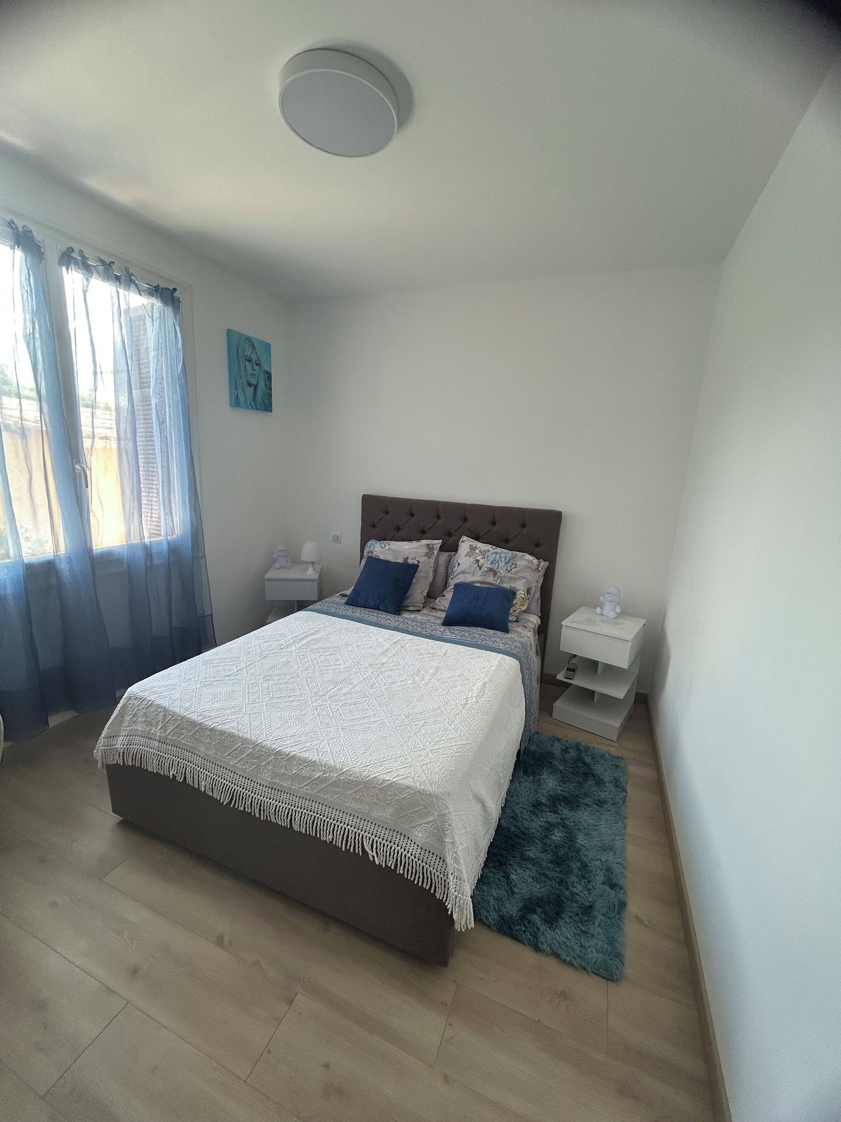 Une chambre à coucher avec un lit, une table de chevet, une horloge murale et une fenêtre avec des rideaux.