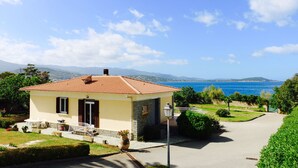 Ein kleines Haus mit rotem Ziegeldach, Steinaußenwand und Blick aufs Meer.