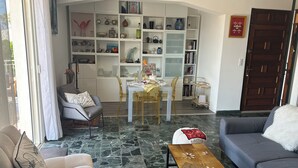 Ein Wohnzimmer mit einer Couch, einem Esstisch mit Stühlen, einem Bücherregal und einer Tür.