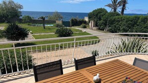 Eine Terrasse im Freien mit einem Holztisch und Stühlen, einem weißen Geländer und Blick auf das Meer.