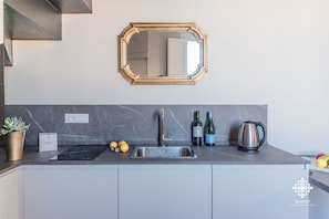 Een moderne keuken met een RVS spoelbak, een marmeren achterwand, een spiegel met gouden lijst en een waterkoker op het aanrecht.
