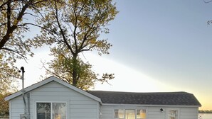 A single-story mobile home with a small porch, a window, and a trash can.