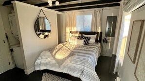 A bedroom with a bed, a mirror, a window with curtains, a door, and a wall-mounted heater.