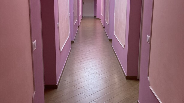 En lång, smal hall med rosa väggar och trägolv.