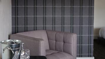 A corner of a room with a grey upholstered armchair, a metal bucket, and a glass on a black table.