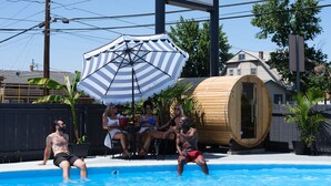 A swimming pool with a wooden sauna, a striped umbrella, and a fence. - Motolodge (Pendleton)