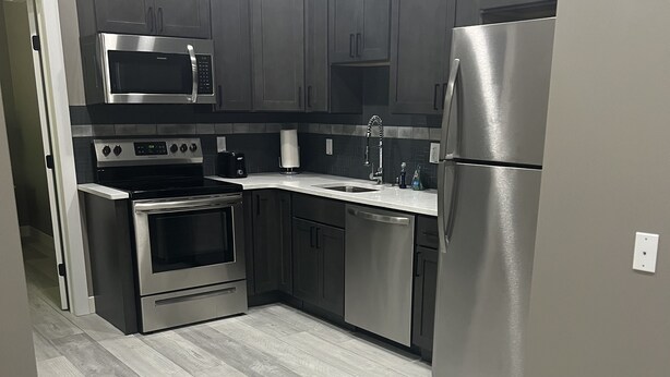A modern kitchen with grey cabinets, stainless steel appliances, and a herringbone-patterned floor.