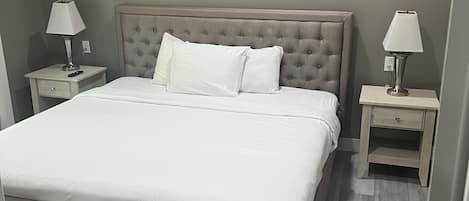 Una cama bien hecha con sábanas blancas, dos mesitas de noche con lámparas y un cabecero capitonado.