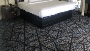 A hotel room with a large bed, two bedside tables with lamps, a TV, and a patterned carpet. - Niagara Crossing Hotel and Spa King Room (Lewiston)