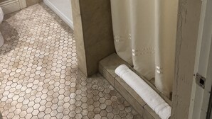 A bathroom with hexagonal patterned floor tiles, a white bathtub, and a beige shower curtain. - Niagara Crossing Hotel and Spa King Room (Lewiston)
