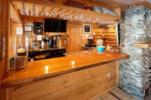 Uma área de bar com balcão de madeira, parede de pedra, um recipiente azul e um quadro de menu.