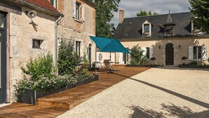 Un patio con cubierta de madera, zona de grava y un edificio de techo a la vista y paredes de piedra.