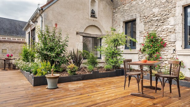 Un patio con cubierta de madera, plantas en macetas y mobiliario exterior.