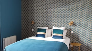 Une chambre à coucher avec un lit, des murs bleus, un papier peint à motifs, une petite table de chevet et un luminaire suspendu.
