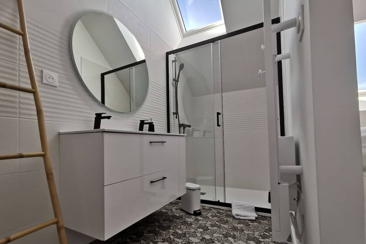 Uma casa de banho moderna com toucador branco, espelho redondo, cabine de duche em vidro e chão estampado.