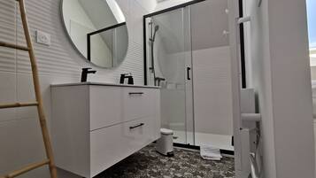 A modern bathroom with a white vanity, a round mirror, a glass shower enclosure, and a patterned floor.