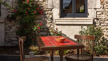 Une table en bois placée à l’extérieur, avec un saladier, deux chaises et, en arrière-plan, un mur de pierre orné de plantes grimpantes.