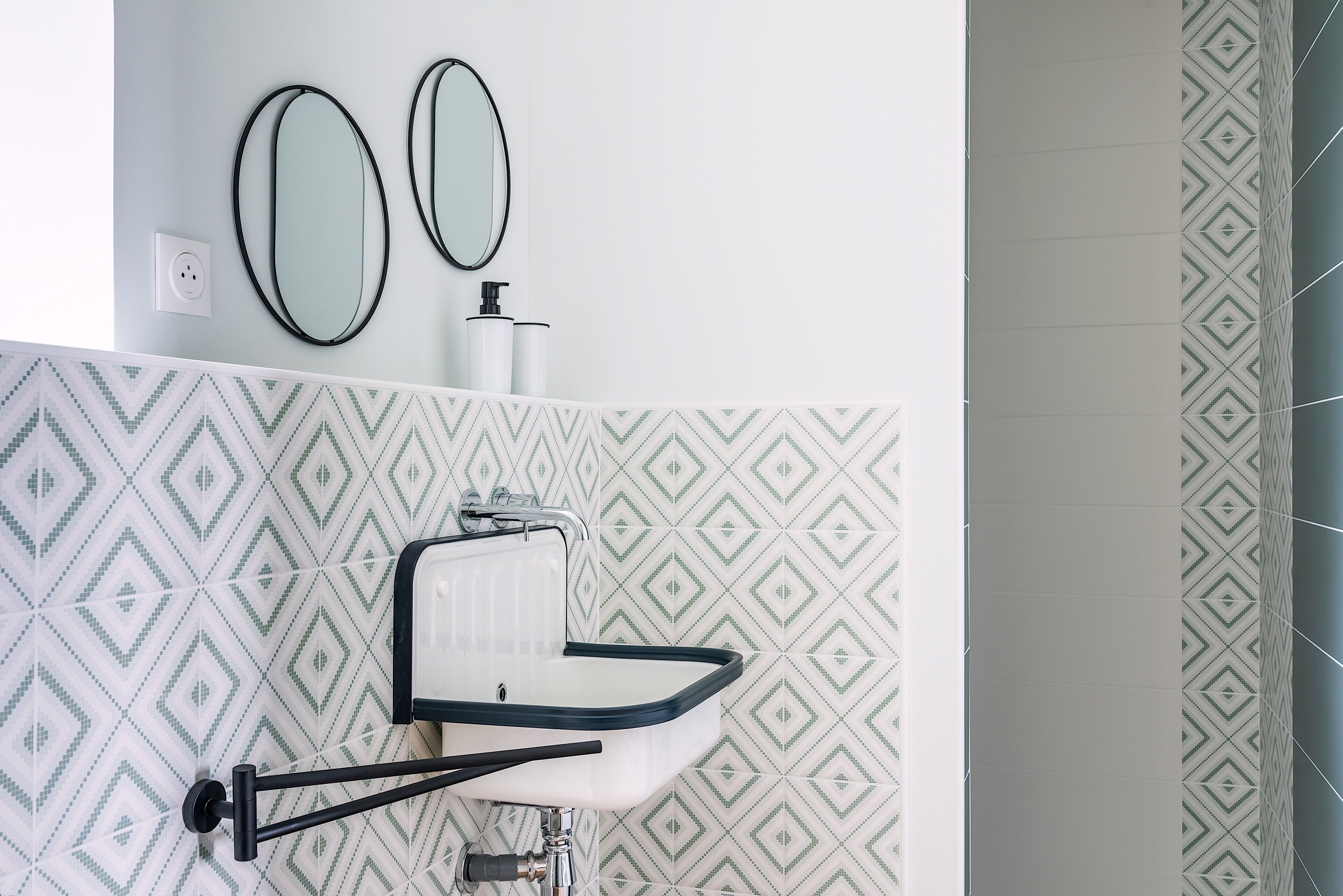 A bathroom with a white sink, two mirrors, and patterned tiles.