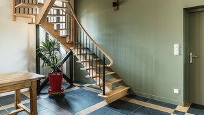 Una escalera con escalones de madera y barandillas negras, una planta en maceta roja y un suelo con estampado de cuadros.