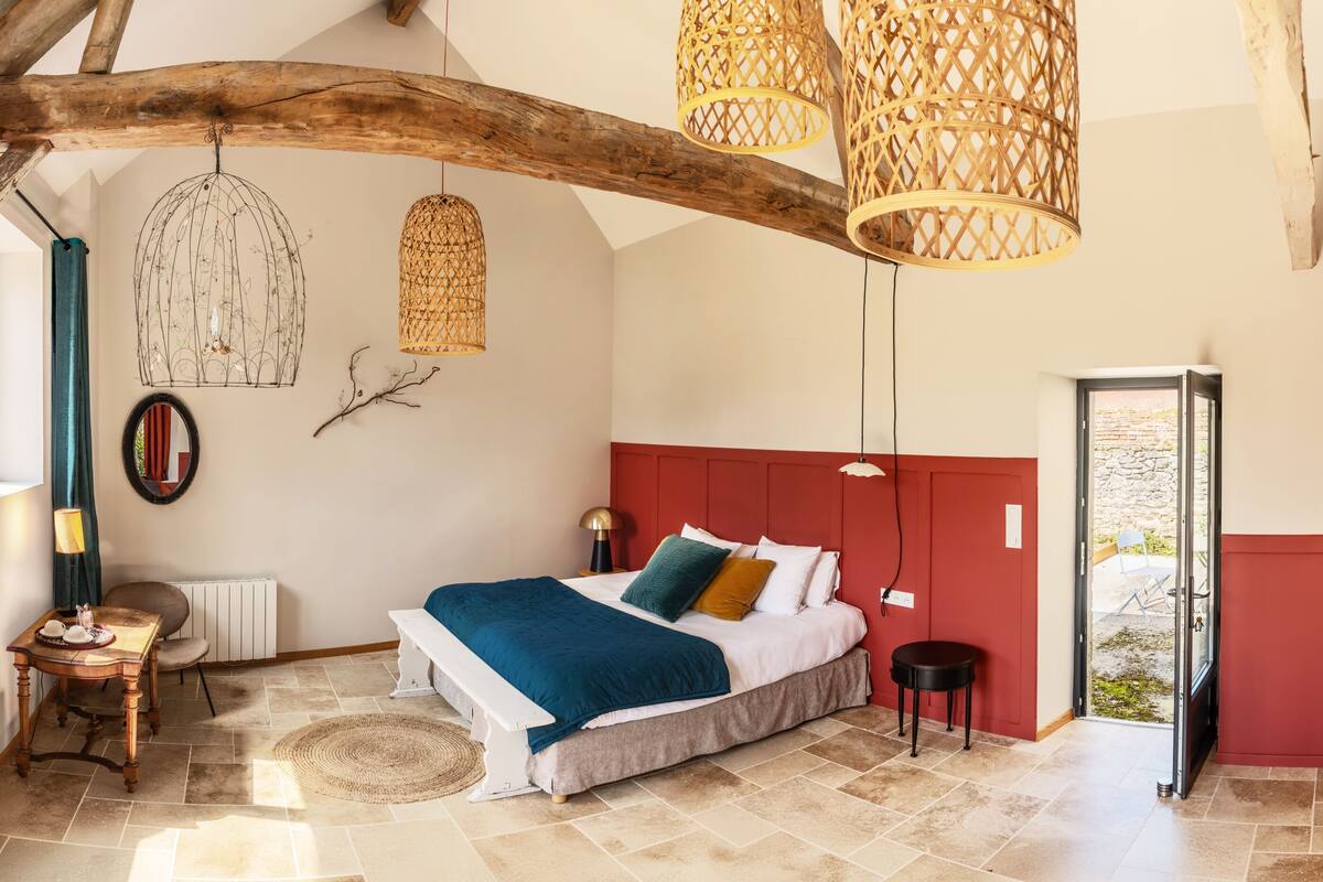 Quarto com uma cama grande, uma viga de madeira no teto e vista através de uma porta de vidro.