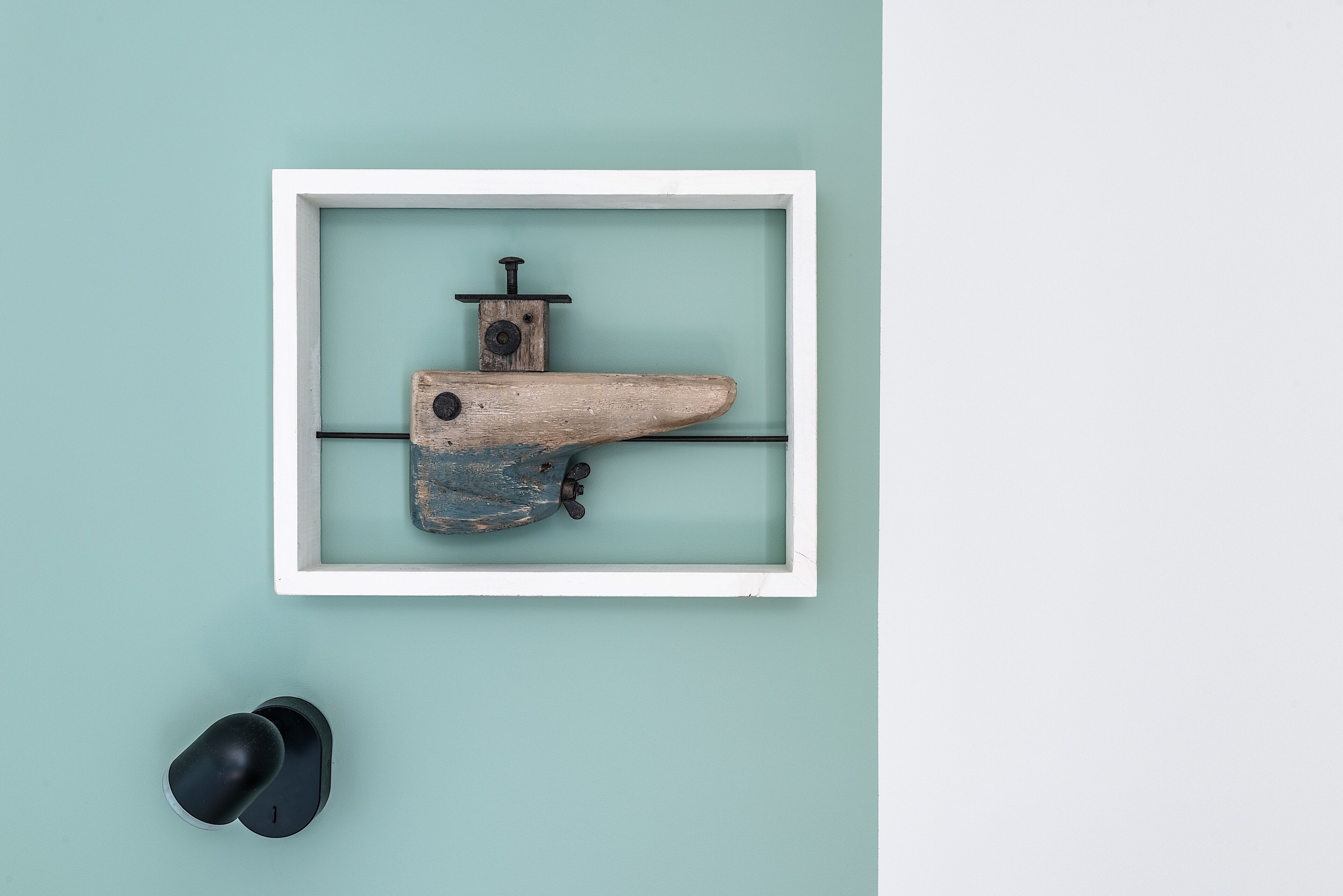 Un objet rustique encadré, doté d’un manche en bois et de pièces métalliques, fixé sur un mur de couleur turquoise.