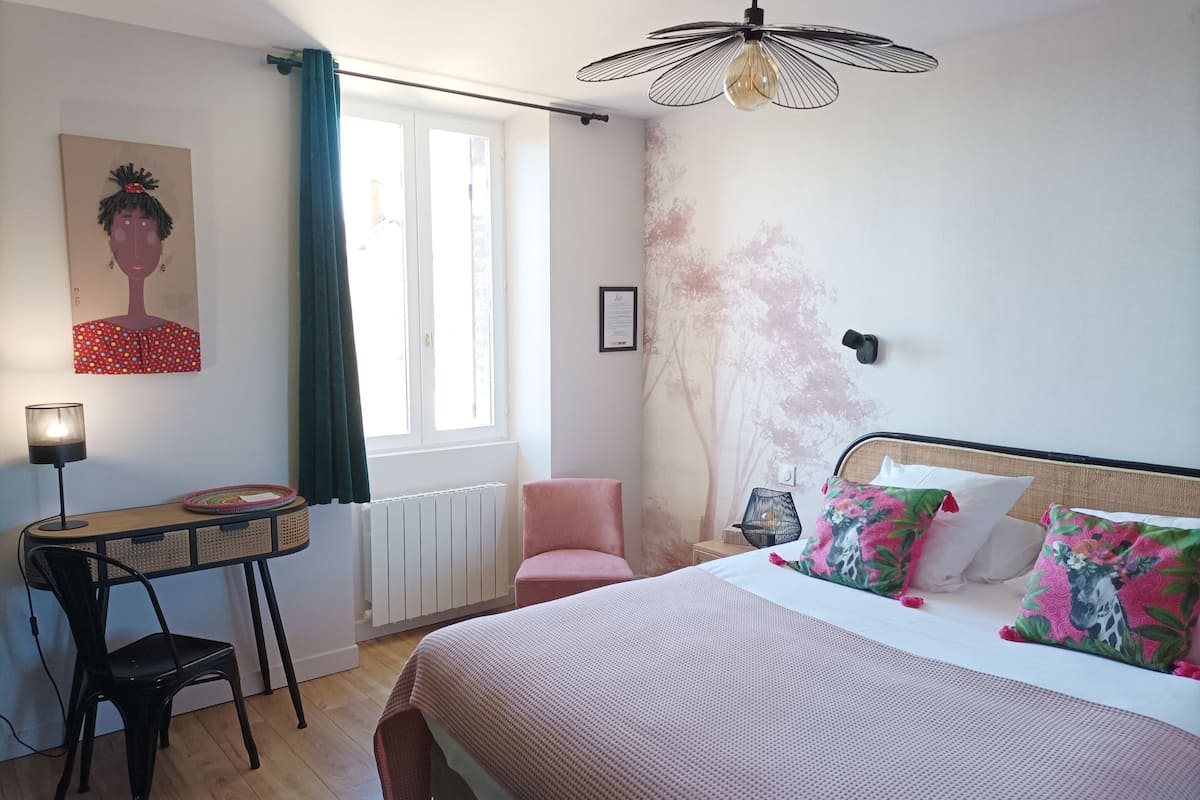 Um quarto com cama, escrivaninha, cadeira, radiador e janela com cortinas.