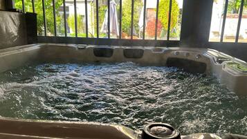 A hot tub with visible bubbles, surrounded by metal bars and a view of greenery and buildings.