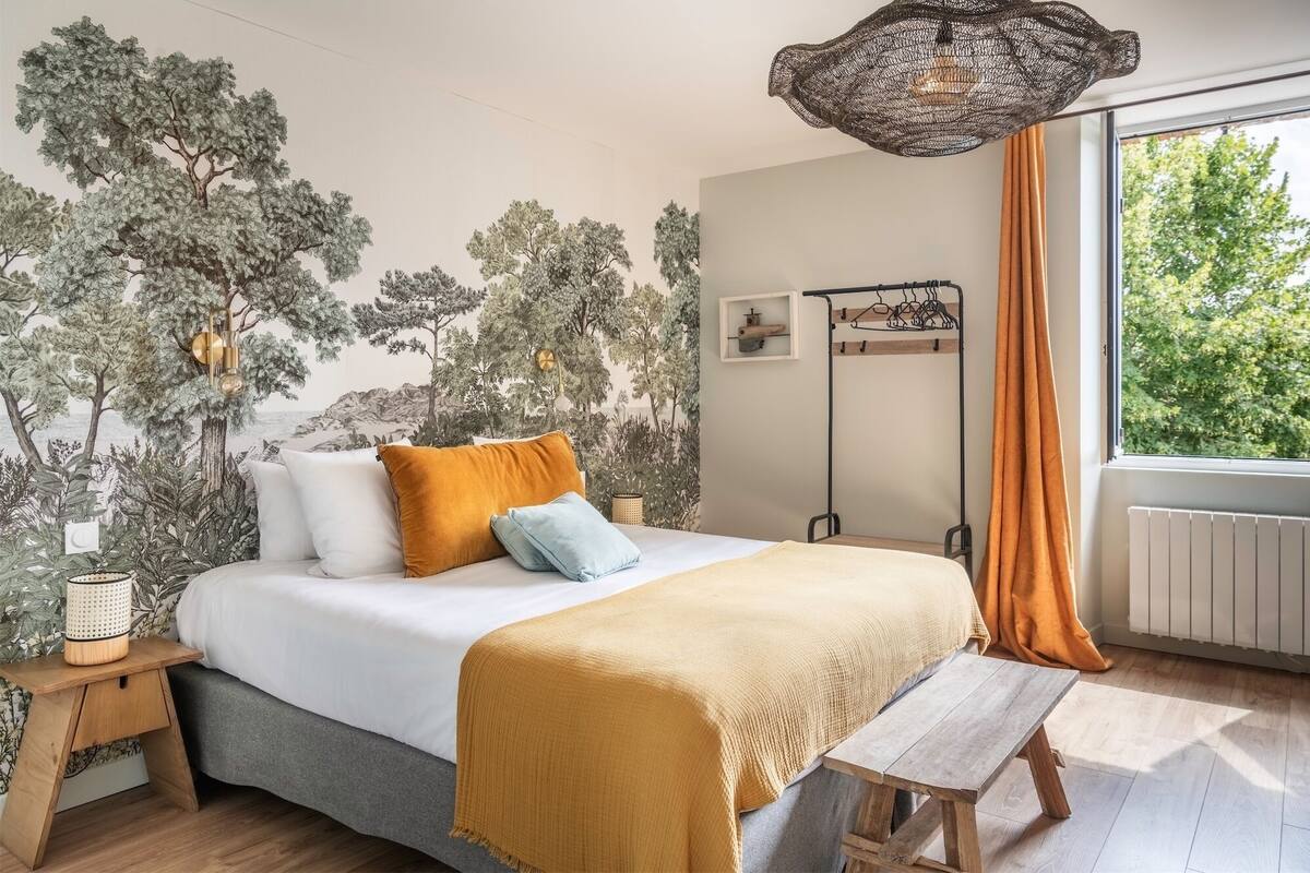 Quarto com cama, mesa de cabeceira, luminária pendente, radiador e janela com cortinas.