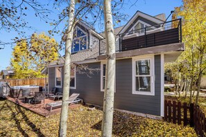 A two-story house with a balcony, a patio with outdoor furniture, and a wooden fence. - Home in Downtown Breck w/ private hot tub, fireplace, and walkable to Main St (Breckenridge)