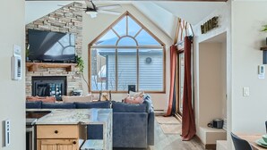 A spacious living area with a fireplace, a large window, and a modern kitchen. - Home in Downtown Breck w/ private hot tub, fireplace, and walkable to Main St (Breckenridge)