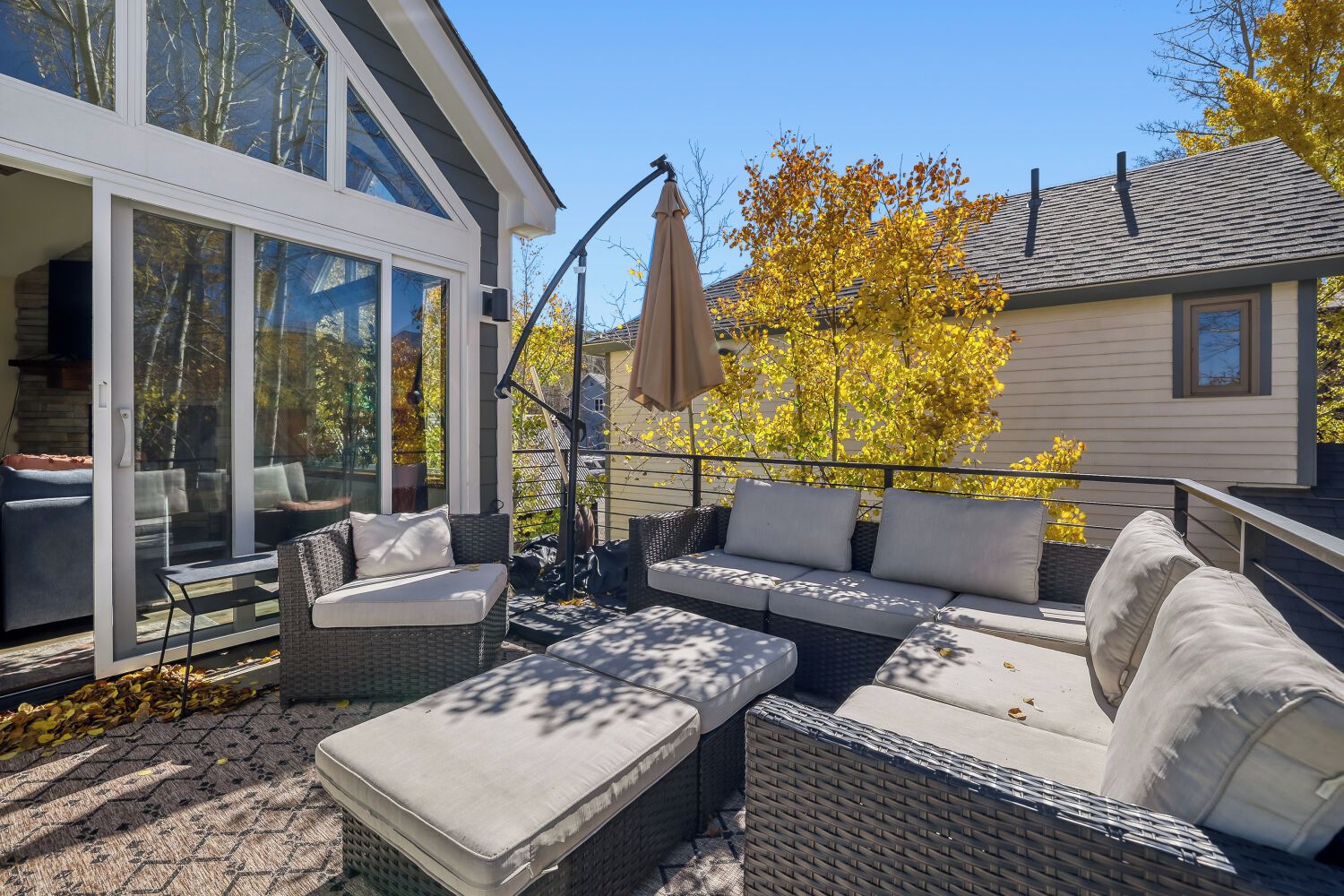 An outdoor patio with wicker furniture, a glass door leading to a room, and a tree with yellow leaves.