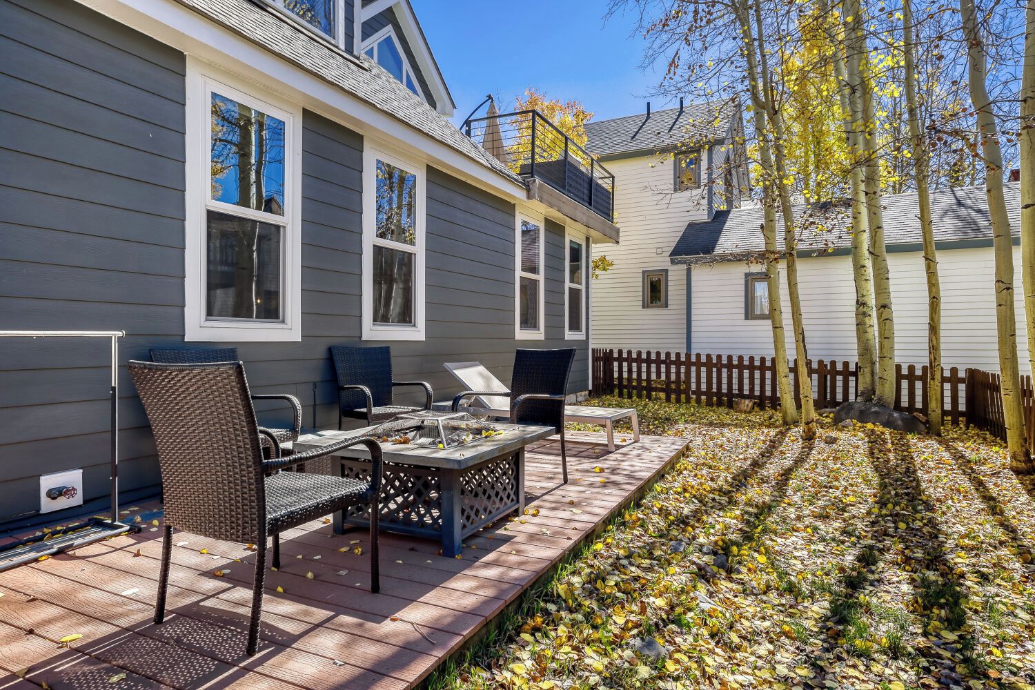 Eine Terrasse mit Tisch und Stühlen, ein Holzdeck und ein umzäunter Garten mit Bäumen.