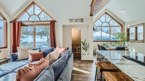 A modern living room with a large blue sofa, a wooden bench, and a marble kitchen island. - Home in Downtown Breck w/ private hot tub, fireplace, and walkable to Main St (Breckenridge)