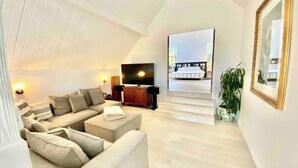 Una sala moderna con un sofá modular, un televisor de pantalla plana y una escalera que lleva a un dormitorio.