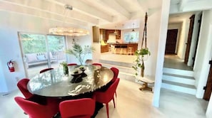 Un espace repas moderne avec une table ronde et des chaises rouges, une cuisine en arrière-plan et un escalier menant à un autre niveau.