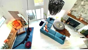 Un vaste espace de vie agrémenté d’un canapé bleu, d’un fauteuil suspendu, d’une cheminée et d’un mur en pierre.
